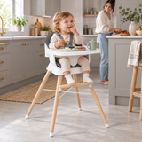 18-month-old toddler self-feeding in grey wooden baby high chair with mum in kitchen background