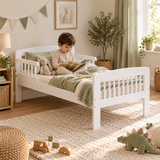 Three-year-old boy reading a picture book in a white wooden toddler bed with sage bedding