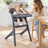 Mum feeding 10 month old baby in dark grey highchair in modern white kitchen