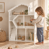 Four-year-old girl playing with a doll beside the white dolls’ house bookcase.