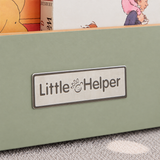 A close-up of a sage green portable bookcase featuring Little Helper logo plaque in brushed steel