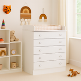 Nursery room with white dresser, shelves, and toys in a bright room.