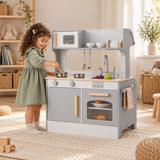 Child stirring a saucepan at a grey wooden toy kitchen in a neutral playroom.