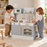 Two children cooking and washing a toy plate at a grey wooden play kitchen.