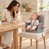 Baby sitting in the grey booster seat secured to a dining chair at the family table.