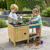Two children playing with a wooden toy mud kitchen set outdoors.