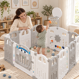 Toddler playing basketball inside a grey and white baby playpen with mum supervising