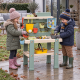 Children playing with an outdoor mud kitchen in winter wearing warm coats, hats and wellington boots