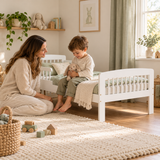 1. Mother beside her toddler sitting on a low white pine bed holding a soft rabbit