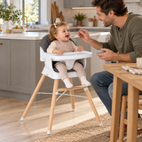 Dad feeding one-year-old baby in grey convertible wooden high chair in a modern family kitchen