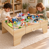 Children playing with a wooden train set on a table in a neutral playroom.