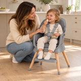 Toddler enjoying a snack in the grey low chair with wooden legs and five-point harness.