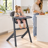18 month old toddler self feeding in dark grey baby high chair with mum in kitchen
