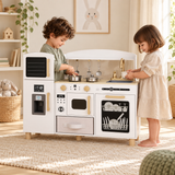 Two three-year-old children cooking and washing up at a white play kitchen in a neutral playroom.