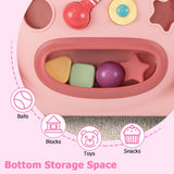 Close-up of a pink children's activity tray with a storage compartment holding colorful toy pieces, plus overlaid icons and Spanish text describing storage capacity for balls, blocks, toys, and snacks.